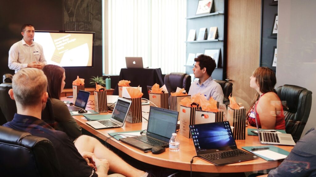 Teamvergadering met meerdere mensen die langdurig stilzitten achter laptops rond een vergadertafel.