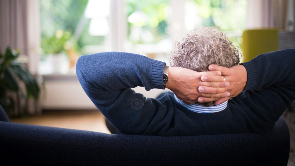 Man geniet van comfort in huis, ontspannen op bank met handen in nek