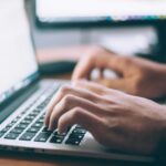 Handen typen op een laptop tijdens het schrijven van een toegankelijke techtekst in een werkomgeving.