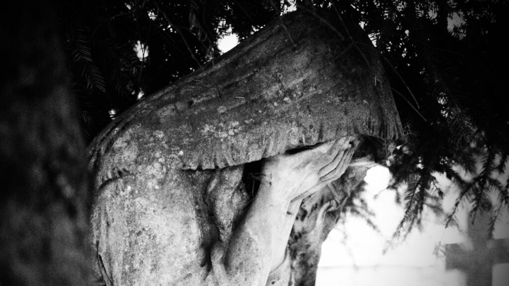 Beeld van rouwende figuur met bedekt gezicht drukt intens verdriet en verlies van nabestaanden uit.